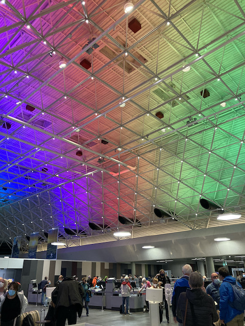 混み合う空港の手荷物検査場、高い天井が虹色に照らされている