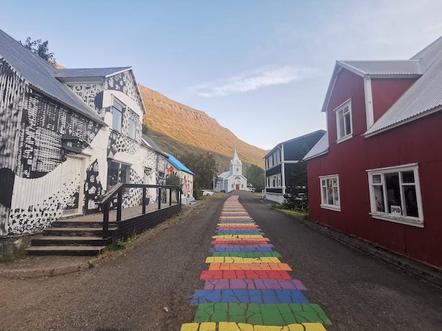 山の前に立つ水色の教会に向かって、虹色に塗られた道