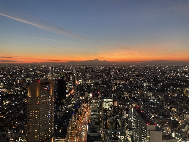 夕焼け空に影になって浮かび上がる富士山と、渋谷の高層ビル街の夜景