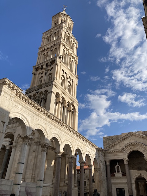 ローマ時代の建築様式を感じる門と円柱の横に、大聖堂の高い塔がそびえている