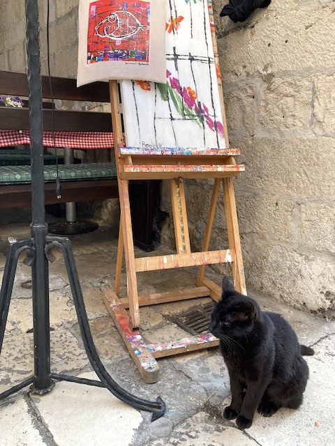 イーゼルに置かれたアート作品の下にちょこんと座っている黒猫