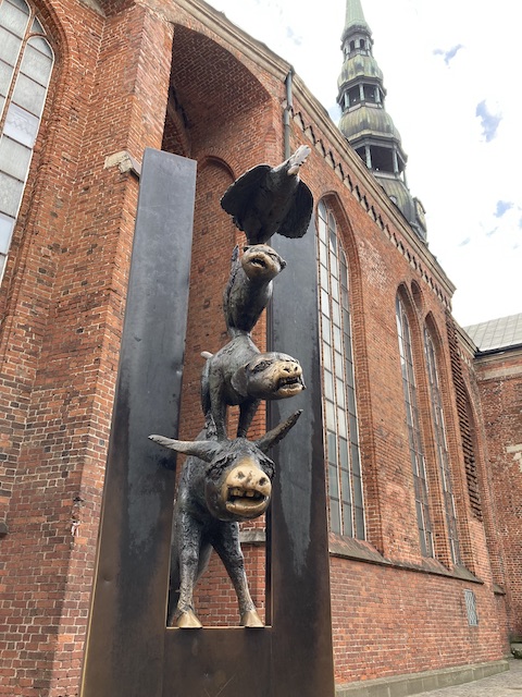 赤煉瓦造りの教会の前に立つ、歪んだ表情のニワトリ、猫、犬、ロバの銅像