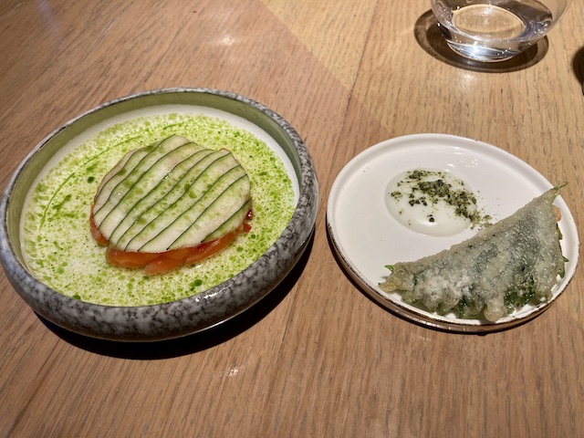 石のような質感の丸い深皿に入ったトラウトと、白い平皿にのった二つ折りの葉っぱと緑の粉がかかった白いソース