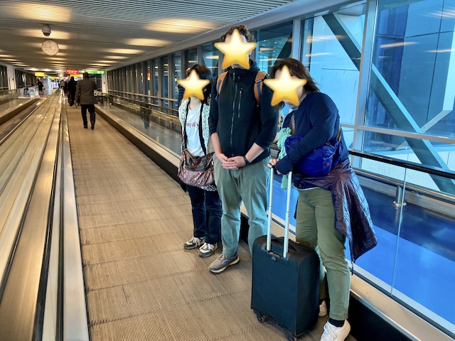 空港内の動く歩道に立っている日本人女性2人とドイツ人男性1人