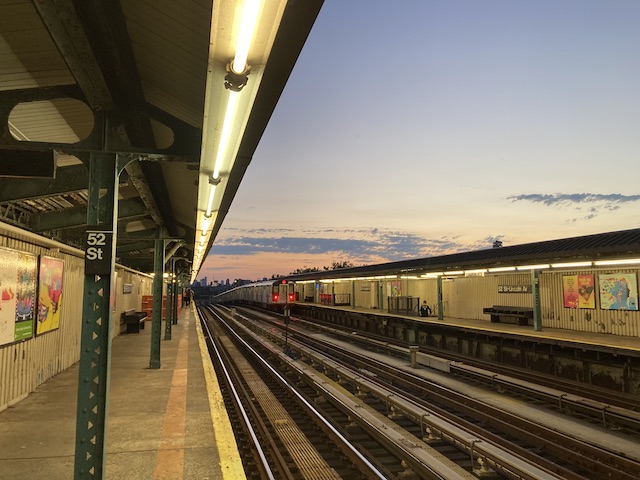 地上を走っているメトロの駅の背景で、夕焼けで空がピンク色になっている