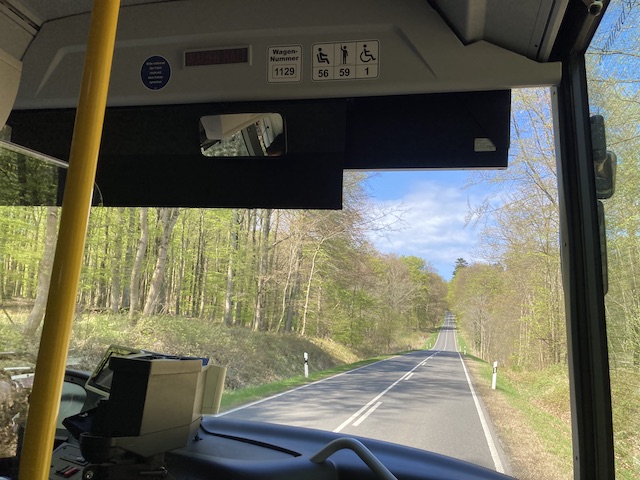バスの最前列の席から見た、森林の中を通っているまっすぐな道路