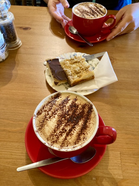 カカオパウダーが掛けられたカプチーノ2つと、四角形に切られたケーキ二種類