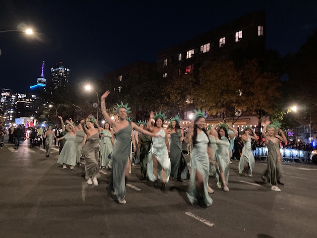 淡いグリーンのドレスに棘のある頭飾りをつけ、観客に手を振る男女のグループ