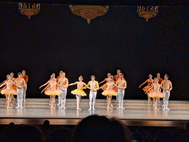 舞台上で拍手を受けてレヴェランスをする、クラシックな衣裳を着た男女のバレエダンサー