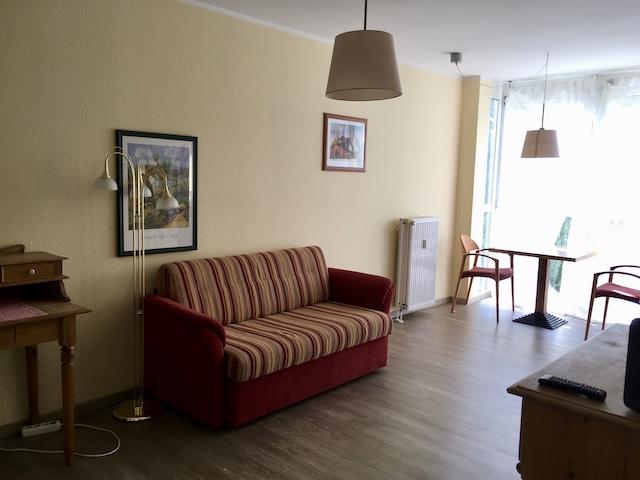 赤い布地のソファが中央に置かれ、窓際にテーブルと二脚の椅子がある