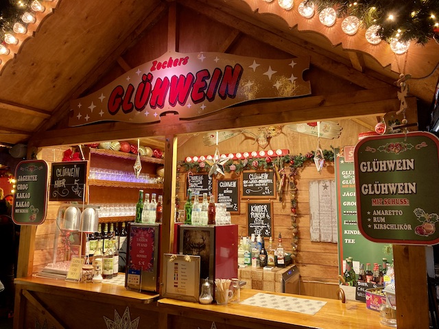 グリューワインなどのメニューが黒板に書かれた、煌びやかなライトのコテージ風のスタンド