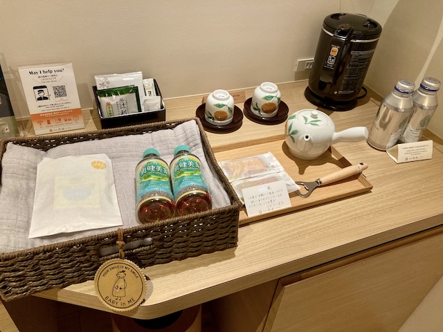 ホテルの部屋の一角に並べられた、水のボトル、湯沸かし器、急須、湯呑み、ティーバッグなど